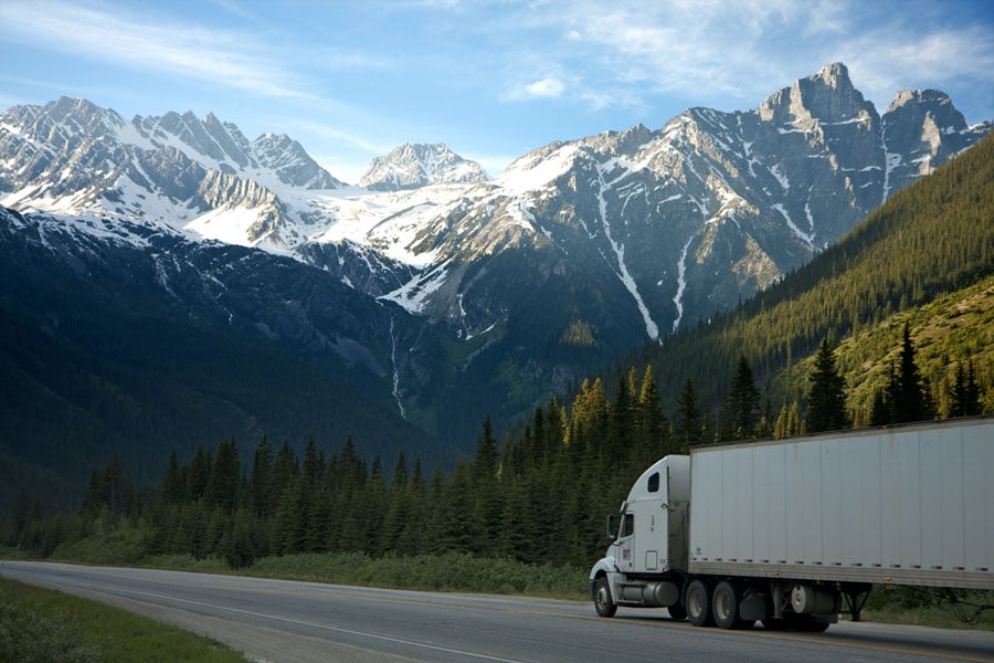 A semi-truck driving in front of mountains.